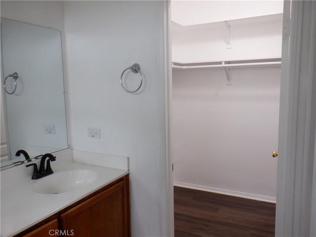 bathroom with baseboards, wood finished floors, a walk in closet, and vanity