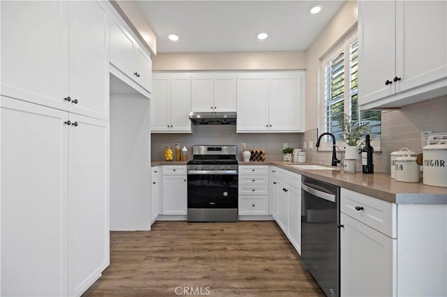 kitchen with appliances with stainless steel finishes, wood finished floors, extractor fan, white cabinetry, and a sink