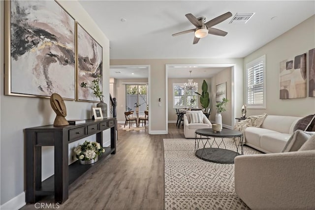 living area featuring baseboards, visible vents, wood finished floors, and ceiling fan with notable chandelier