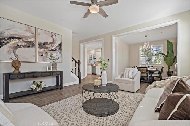 living room with stairs, ceiling fan with notable chandelier, wood finished floors, and baseboards