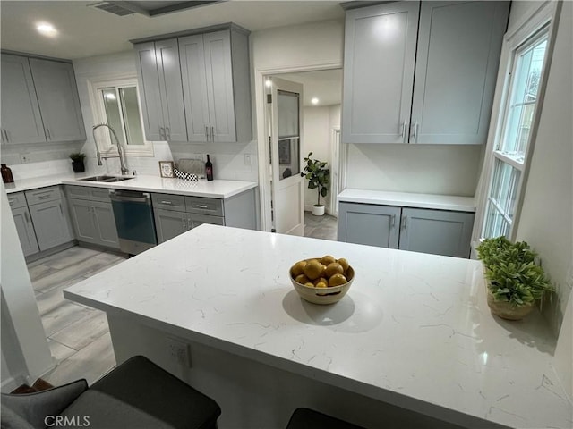 kitchen featuring gray cabinetry, a sink, stainless steel dishwasher, light wood-type flooring, and backsplash