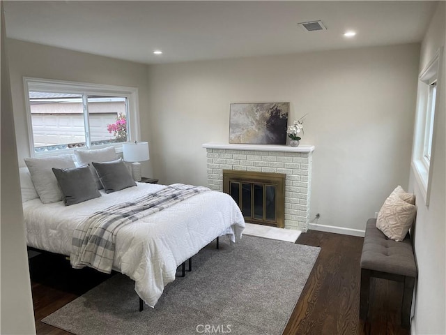 bedroom featuring baseboards, visible vents, dark wood-style flooring, a brick fireplace, and recessed lighting