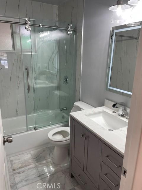 bathroom featuring marble finish floor, shower / bath combination with glass door, vanity, and toilet