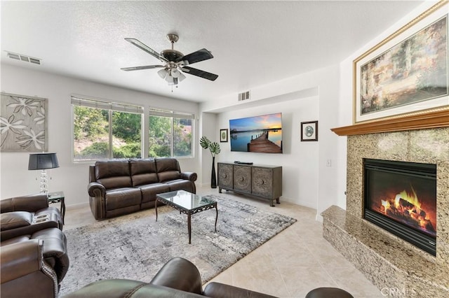 tiled living area featuring ceiling fan, a premium fireplace, visible vents, and a textured ceiling