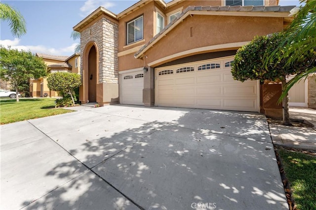 view of front of home with driveway, stone siding, an attached garage, and stucco siding