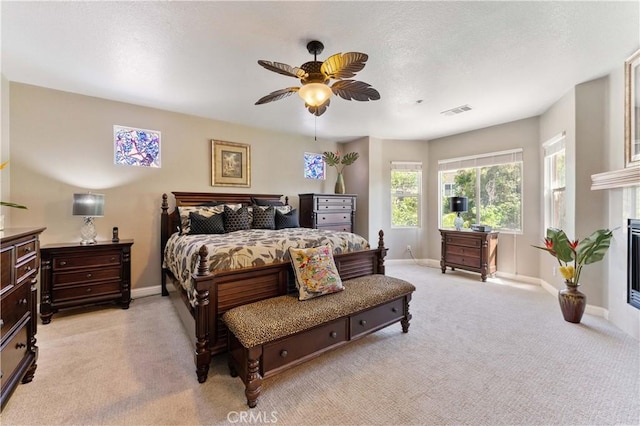 bedroom featuring baseboards, visible vents, a ceiling fan, a glass covered fireplace, and light colored carpet