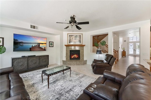 tiled living room featuring visible vents, a ceiling fan, a glass covered fireplace, stairs, and french doors