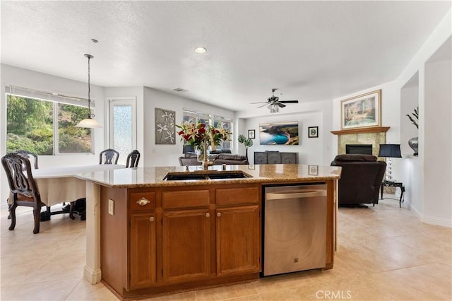 kitchen with a fireplace, a sink, open floor plan, stainless steel dishwasher, and a center island with sink