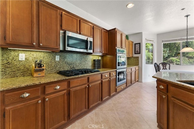 kitchen with decorative backsplash, light stone countertops, stainless steel appliances, pendant lighting, and light tile patterned flooring