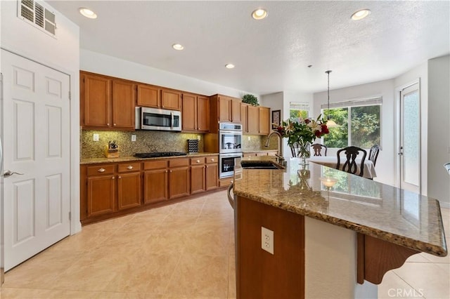 kitchen featuring stainless steel appliances, brown cabinets, visible vents, and a sink