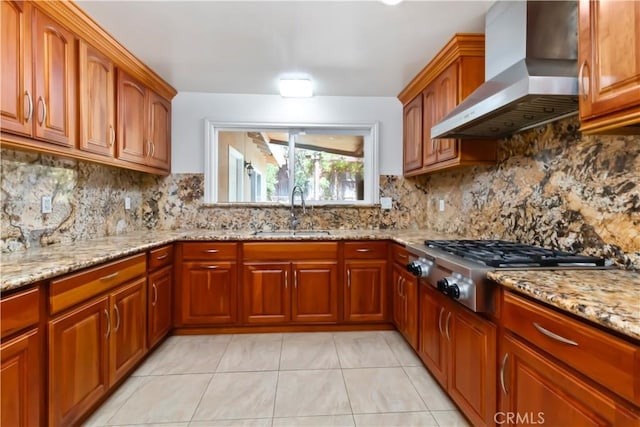 kitchen with stainless steel gas stovetop, a sink, wall chimney exhaust hood, and light stone countertops