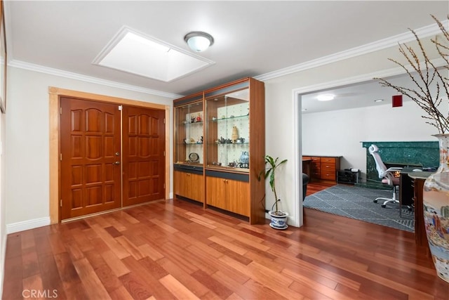 foyer entrance with ornamental molding, a skylight, wood finished floors, and baseboards