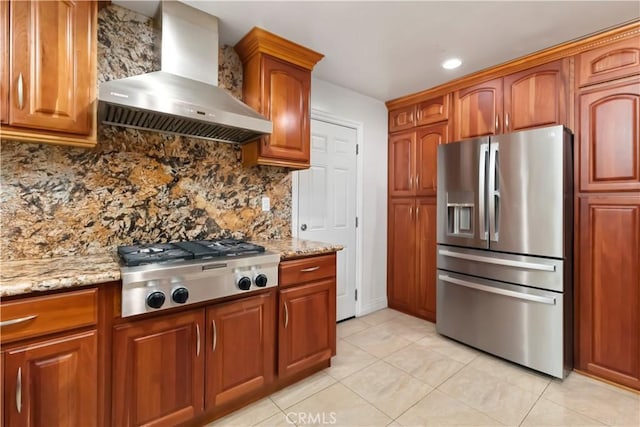 kitchen with light stone countertops, wall chimney exhaust hood, appliances with stainless steel finishes, and decorative backsplash