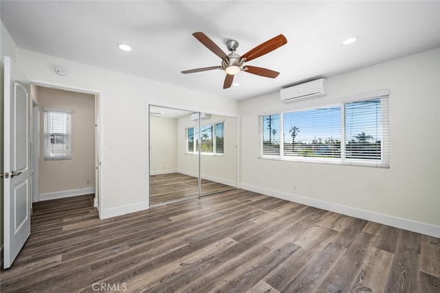 unfurnished bedroom featuring recessed lighting, a closet, an AC wall unit, wood finished floors, and baseboards