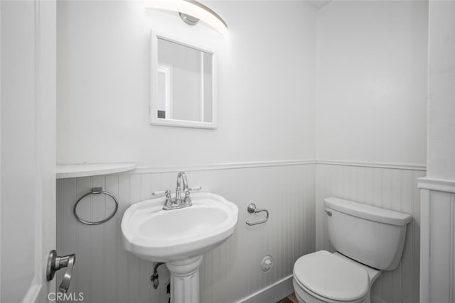 bathroom featuring a wainscoted wall, a sink, and toilet