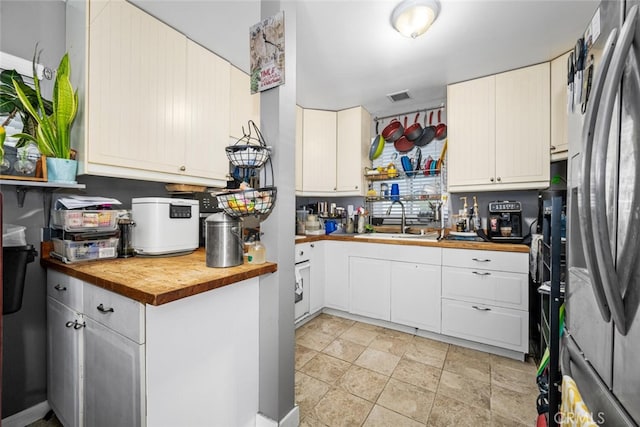 kitchen with visible vents, wooden counters, freestanding refrigerator, white cabinetry, and a sink