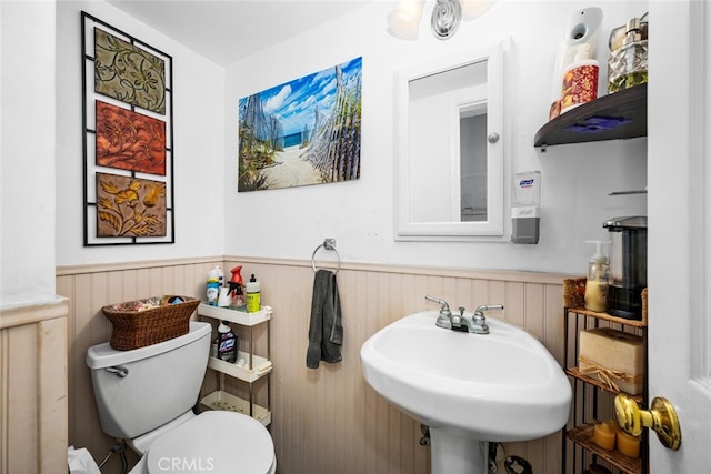 half bathroom with toilet, a wainscoted wall, and a sink