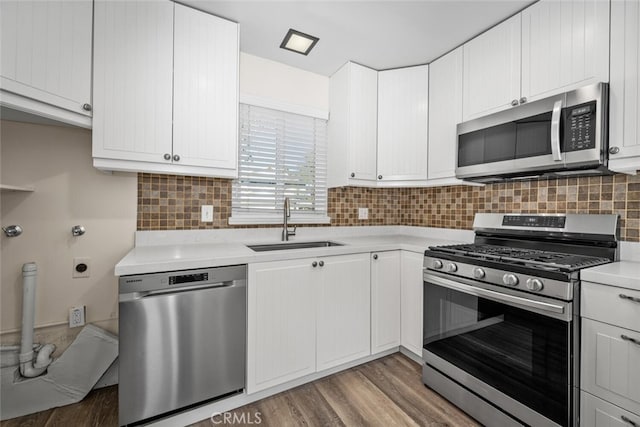 kitchen with light wood-style flooring, stainless steel appliances, a sink, light countertops, and decorative backsplash