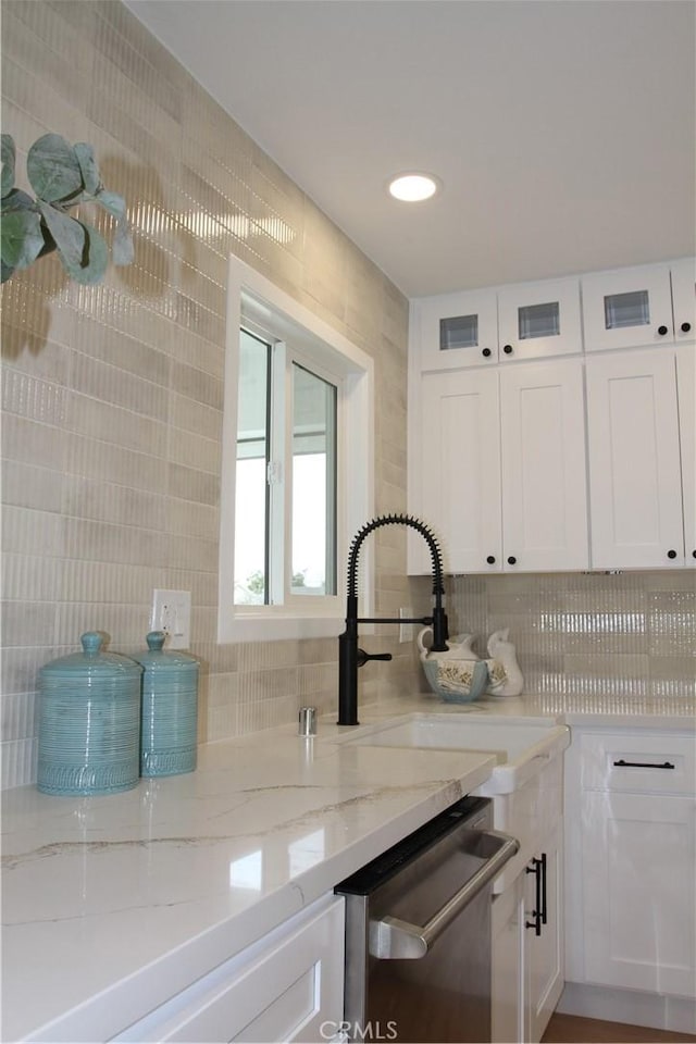 kitchen with decorative backsplash, white cabinets, dishwasher, light stone counters, and a sink