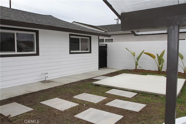 exterior space featuring a shingled roof, fence, and a patio