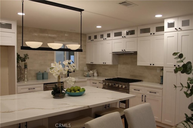 kitchen featuring a breakfast bar area, visible vents, white cabinets, high end stainless steel range oven, and glass insert cabinets