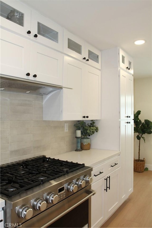 kitchen with light countertops, decorative backsplash, glass insert cabinets, stainless steel gas stove, and white cabinetry