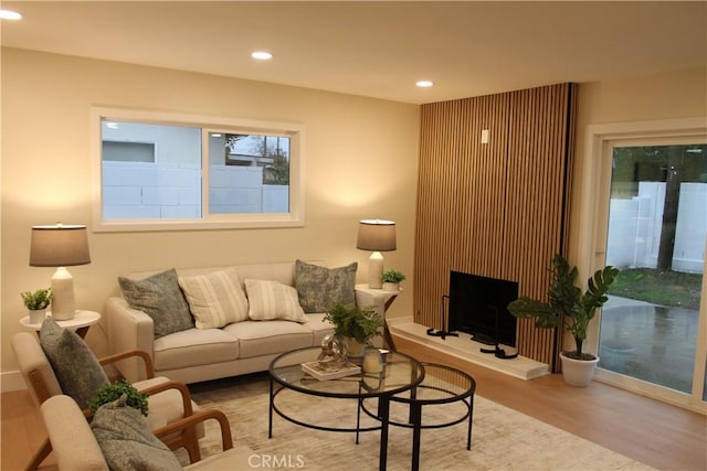 living room featuring recessed lighting, a fireplace with raised hearth, and wood finished floors