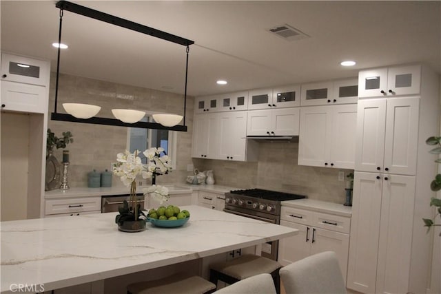 kitchen with a breakfast bar, stainless steel appliances, visible vents, glass insert cabinets, and white cabinets