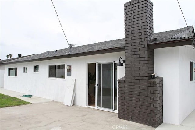 rear view of property featuring roof with shingles, a patio, a chimney, and stucco siding