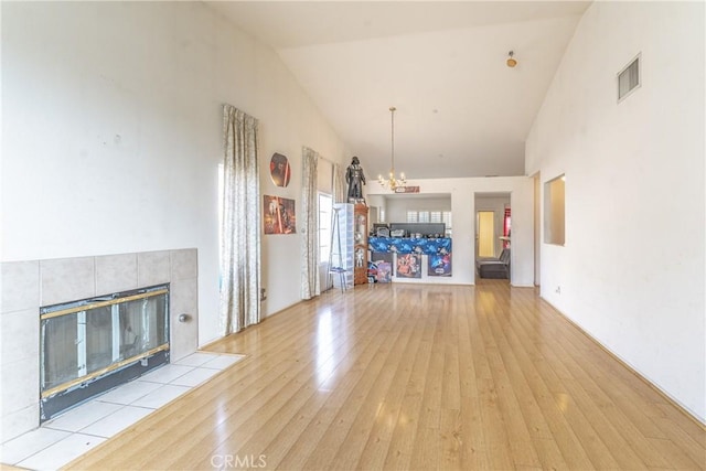 unfurnished living room with light wood finished floors, visible vents, a tile fireplace, an inviting chandelier, and high vaulted ceiling