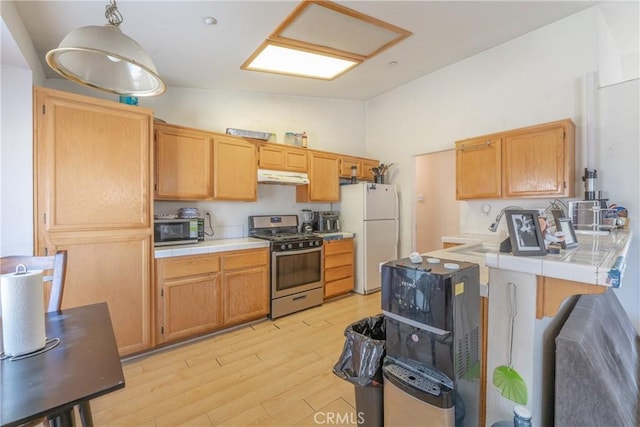 kitchen with tile countertops, stainless steel appliances, lofted ceiling, and under cabinet range hood