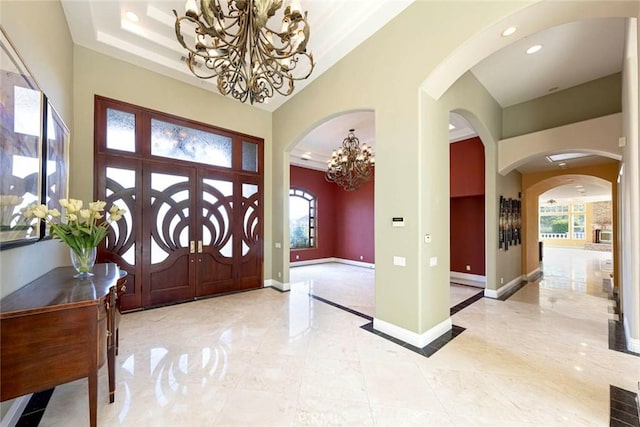 entryway featuring arched walkways, recessed lighting, a notable chandelier, a towering ceiling, and baseboards