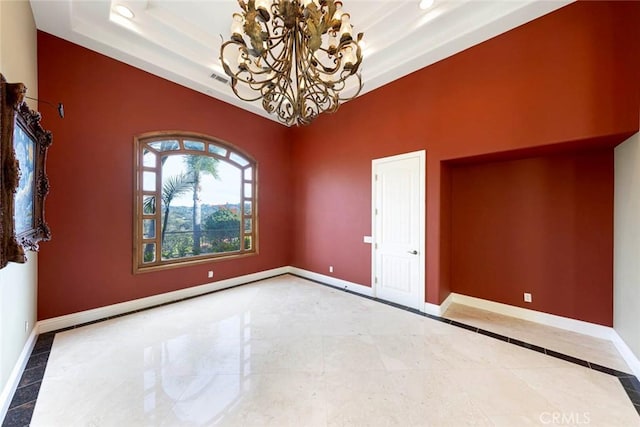 spare room featuring an inviting chandelier, a raised ceiling, and baseboards