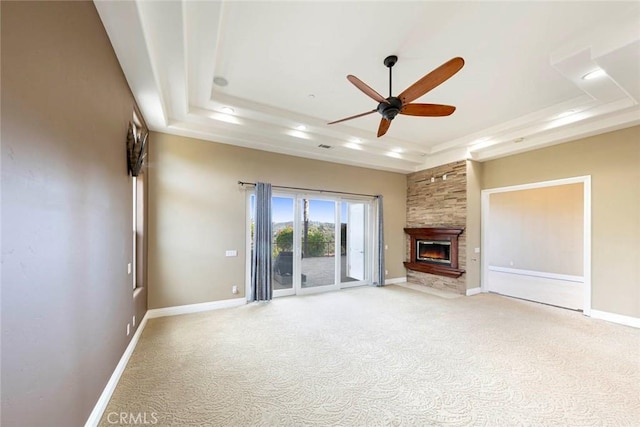 unfurnished living room with light carpet, a tray ceiling, a fireplace, and baseboards