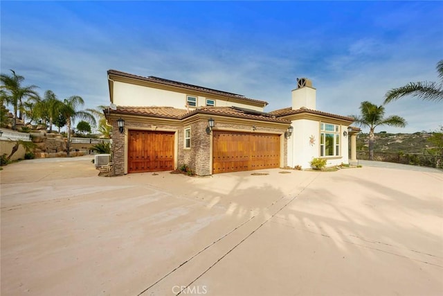 mediterranean / spanish-style house with stone siding, a tile roof, and concrete driveway