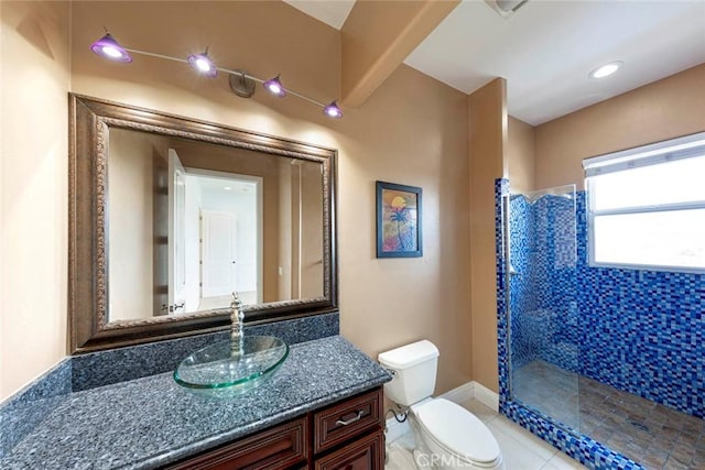 bathroom featuring toilet, a tile shower, vanity, baseboards, and tile patterned floors