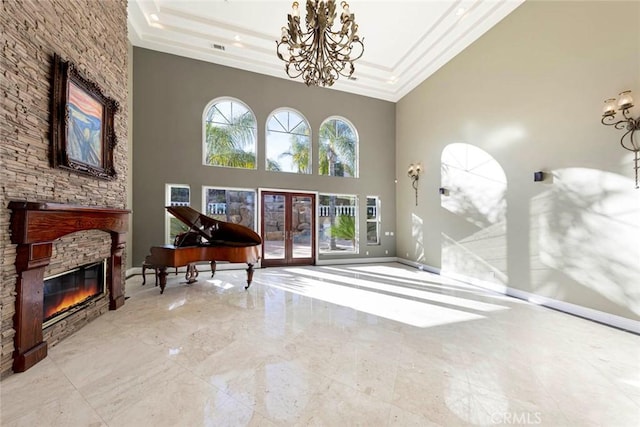 living area with a tray ceiling, french doors, a fireplace, crown molding, and an inviting chandelier