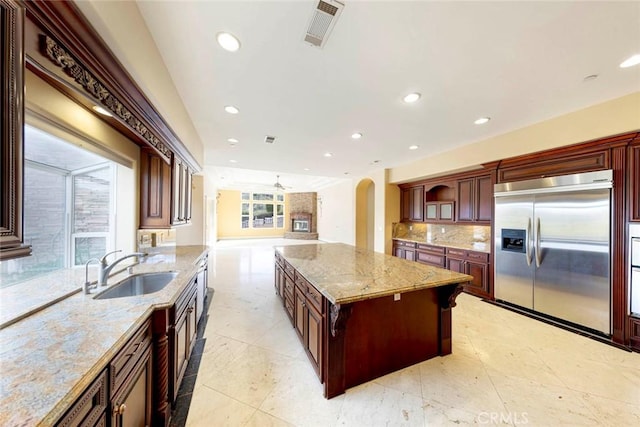 kitchen with arched walkways, a sink, visible vents, backsplash, and stainless steel built in fridge