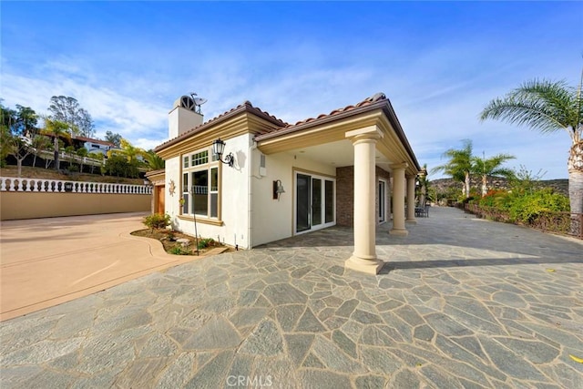 rear view of house featuring a patio area, a tiled roof, a chimney, and stucco siding