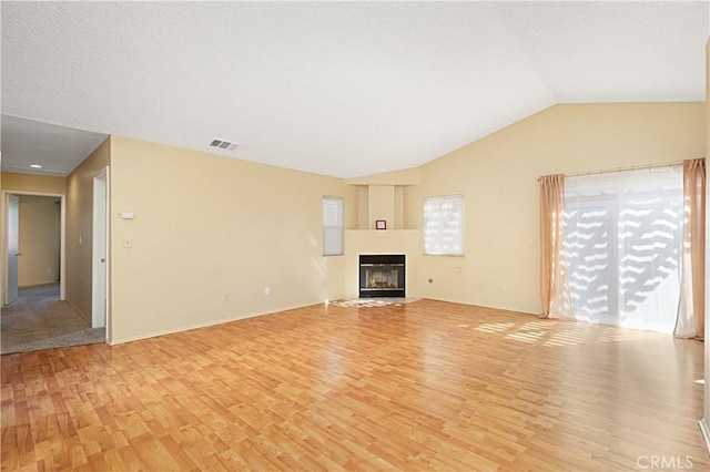unfurnished living room featuring a glass covered fireplace, vaulted ceiling, visible vents, and light wood-type flooring