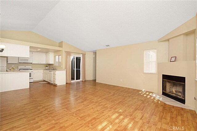 unfurnished living room with visible vents, a fireplace with flush hearth, a sink, vaulted ceiling, and light wood-type flooring