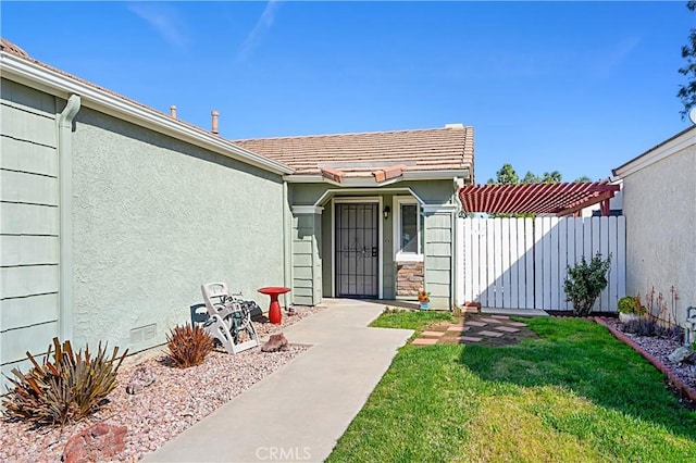 property entrance with stucco siding, a lawn, a tile roof, a pergola, and fence