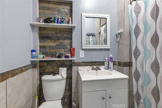 bathroom featuring toilet, vanity, and tile walls