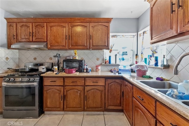 kitchen with brown cabinetry, light countertops, stainless steel gas stove, and under cabinet range hood