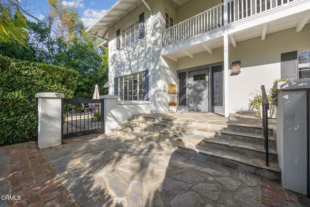 doorway to property featuring a balcony, a gate, and stucco siding