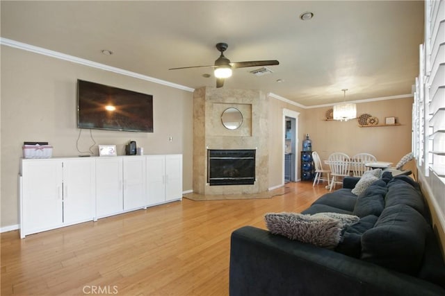 living area featuring crown molding, a fireplace, light wood finished floors, visible vents, and a ceiling fan