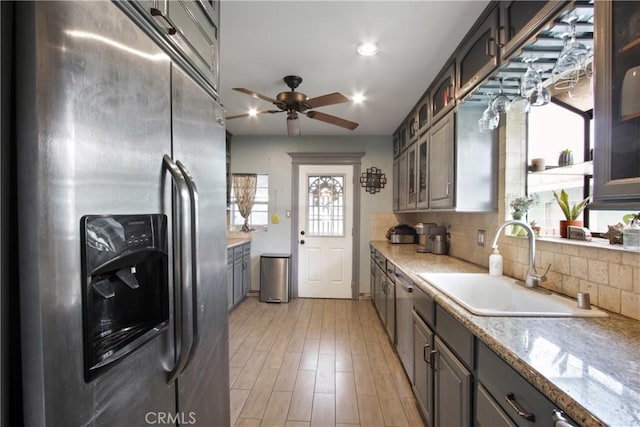 kitchen with light wood finished floors, stainless steel fridge with ice dispenser, glass insert cabinets, a sink, and backsplash