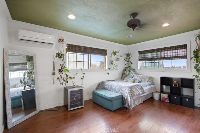 bedroom featuring a textured ceiling, baseboards, wood finished floors, and a wall mounted air conditioner