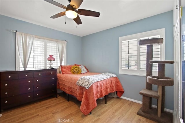 bedroom with baseboards, multiple windows, ceiling fan, and light wood finished floors