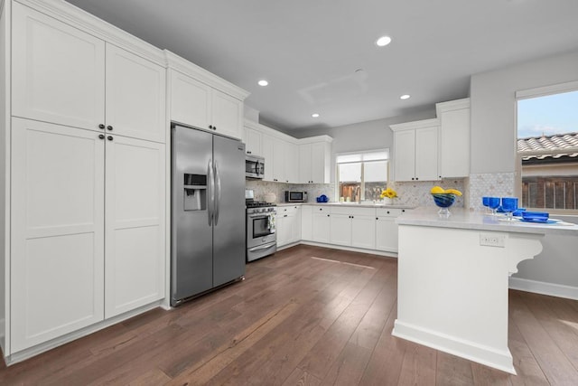 kitchen featuring a peninsula, appliances with stainless steel finishes, dark wood finished floors, and backsplash